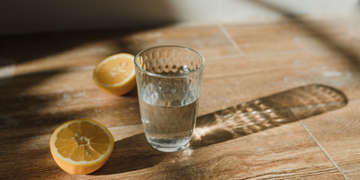 Kozarec vode na leseni mizi. Zraven sta dve limonini rezini.